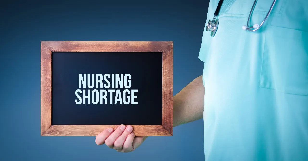nurse holding the nursing shortage sign written on a chalkboard